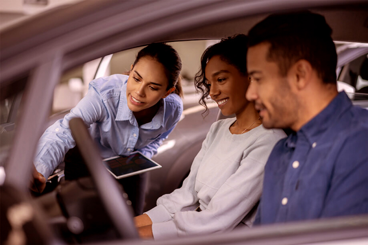 Car sales woman showing features to couple